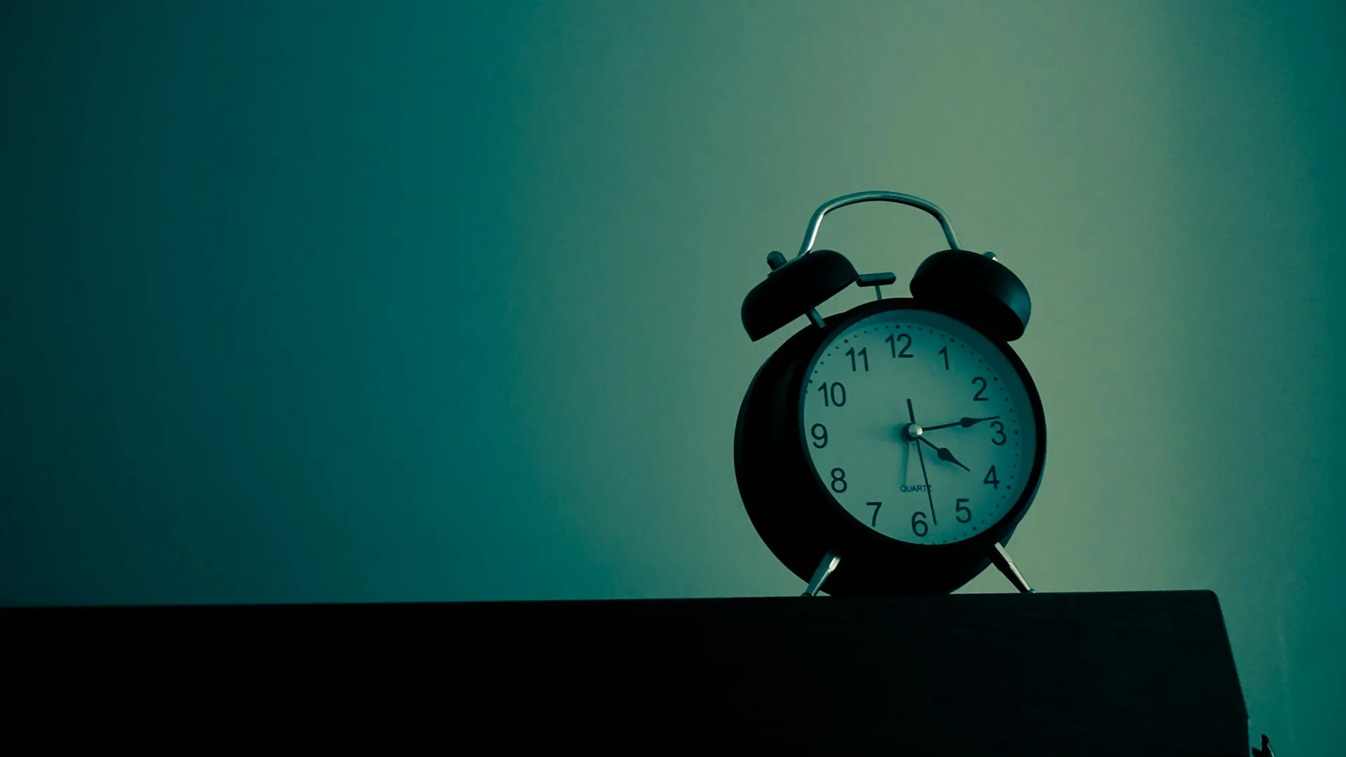 A minimal black-and-white analog alarm clock in soft focus on a nightstand