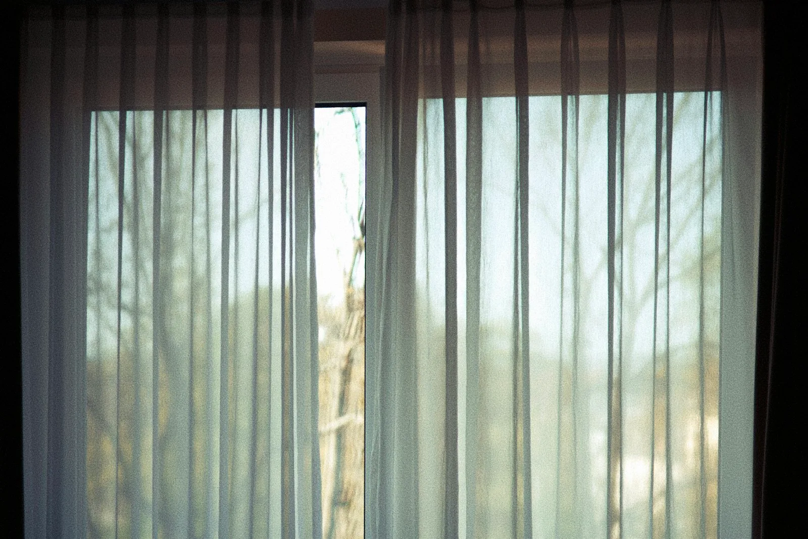 Sheer curtain moving in a breeze from an open window in a cool-toned bedroom at night