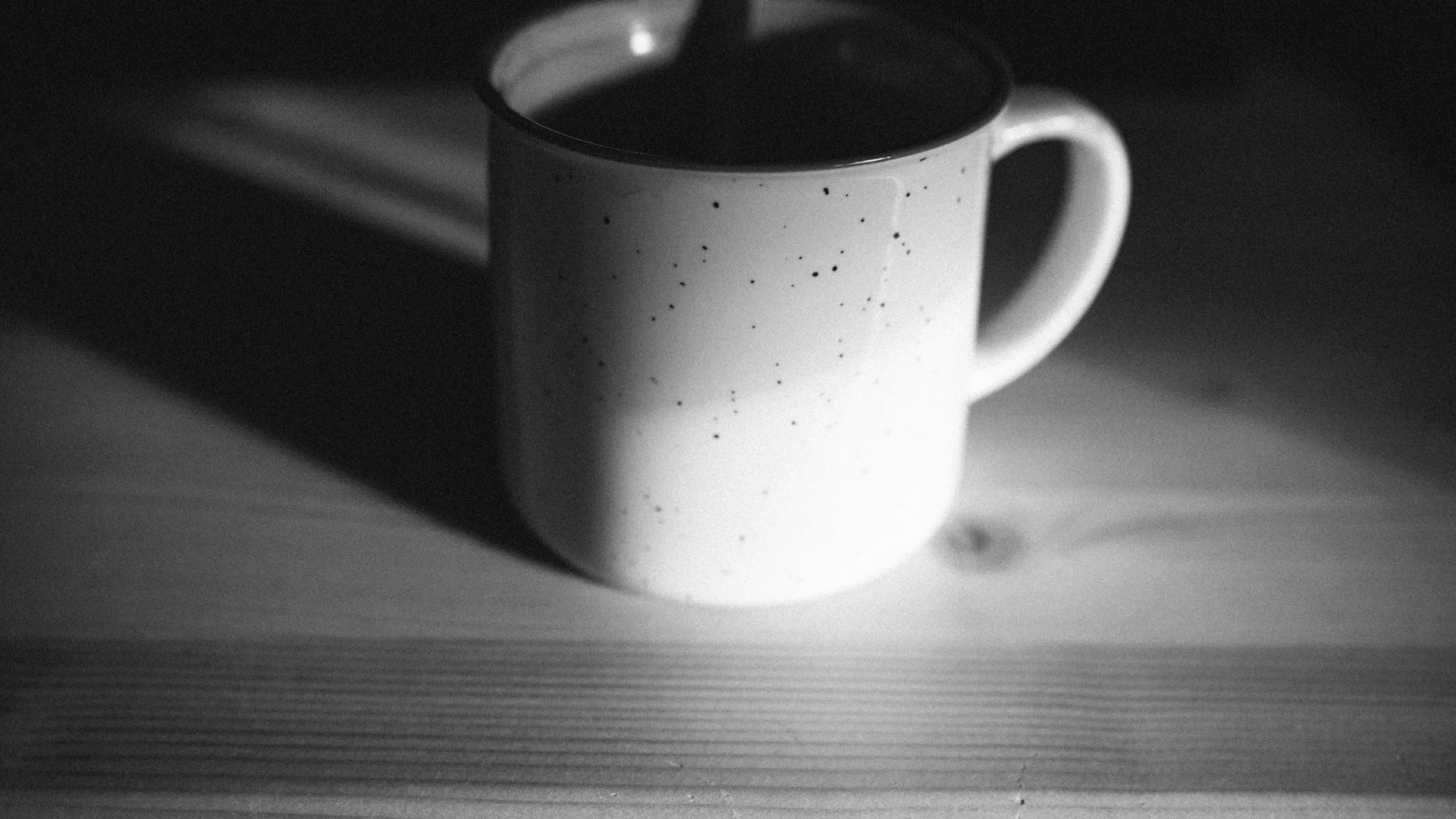 Grayscale coffee mug beside a lit candle in low light