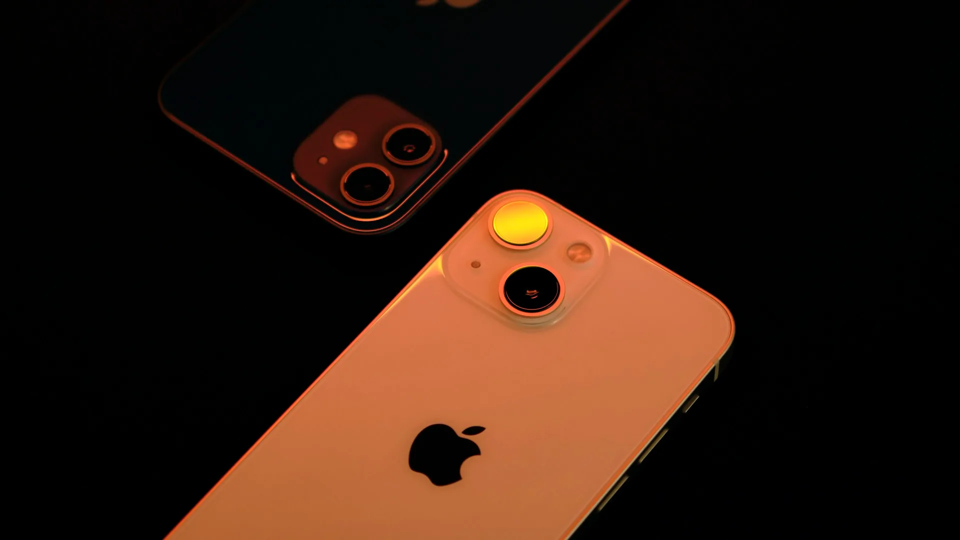 Two iPhones lying next to each other on a dark surface