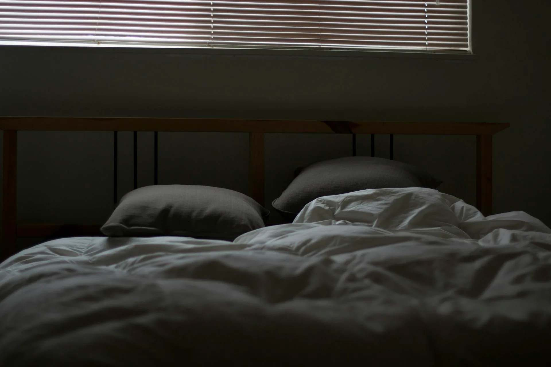 An empty, made bed lit by moonlight through closed blinds