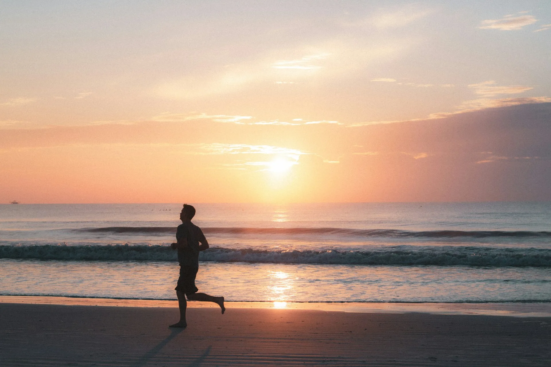 Silhouette of a person running along the beach at sunset