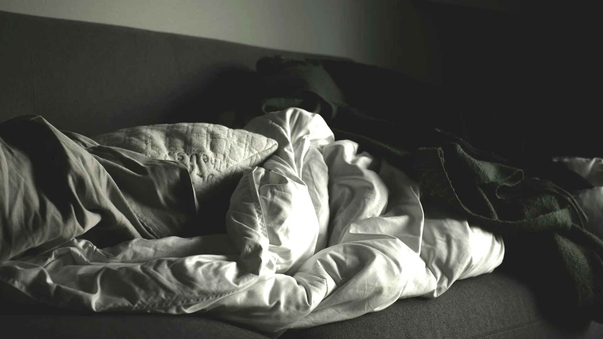 Grayscale crumpled blankets on a sofa, evoking exhaustion