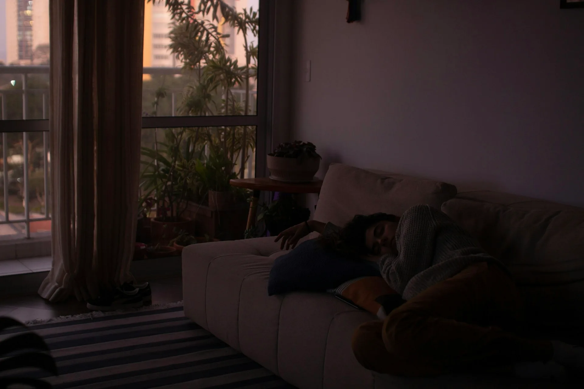 Person napping on a couch in golden-hour light with a city view through the window