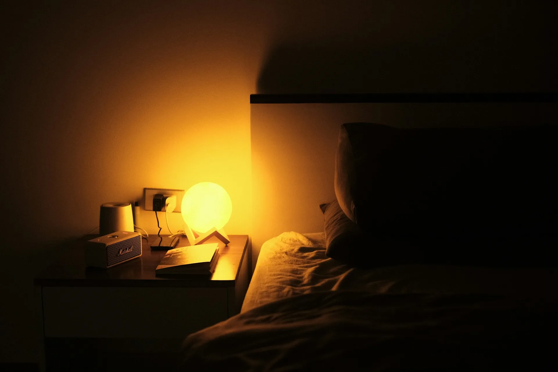 Dimly lit bedroom with a warm bedside lamp, no phone or screen in frame, a book on the nightstand